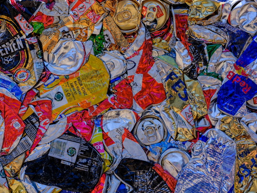 A group of tightly packed black plastic rubbish bags rests on the pavement beside a black metal fence with vertical bars, in an outdoor urban setting. The bags appear to contain household waste and ar